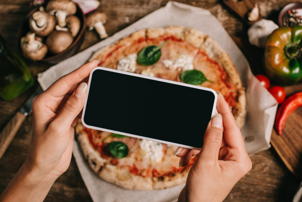 Cropped shot of food blogger taking picture of cooked pizza on baking paper on wooden surface - Photo, Image