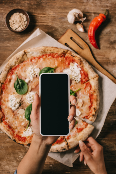木の表面に紙を焼く調理ピザの写真を撮る食品のブロガーのショットをトリミング - 写真・画像