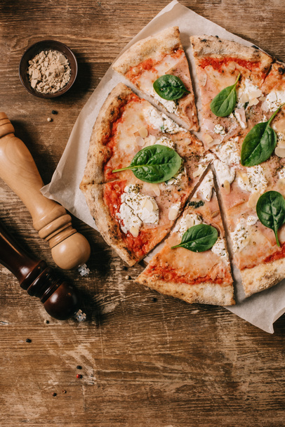 top view of cut italian pizza, salt and pepper grinders on wooden tabletop - Foto, imagen