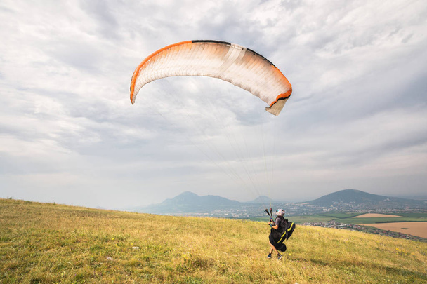 A man paraglider taking off from the edge of the mountain with fields in the background. Paragliding sports - Photo, image