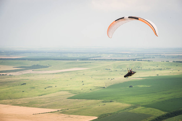 White orange paraglide with a paraglider in a cocoon against the background of fields of the sky and clouds. Paragliding Sports - Zdjęcie, obraz
