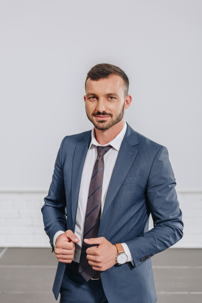 handsome businessman touching jacket and looking at camera in hub - Foto, Imagen