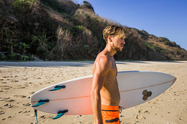 vue latérale de l'homme avec planche de surf regardant loin sur la plage de sable
 - Photo, image
