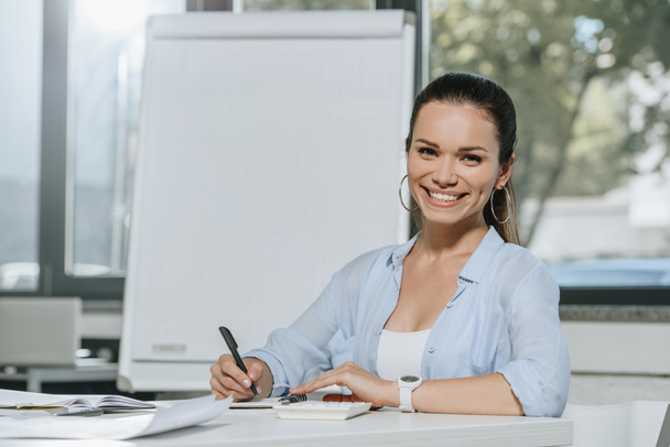 улыбающаяся привлекательная деловая женщина, смотрящая в камеру в офисе
 - Фото, изображение