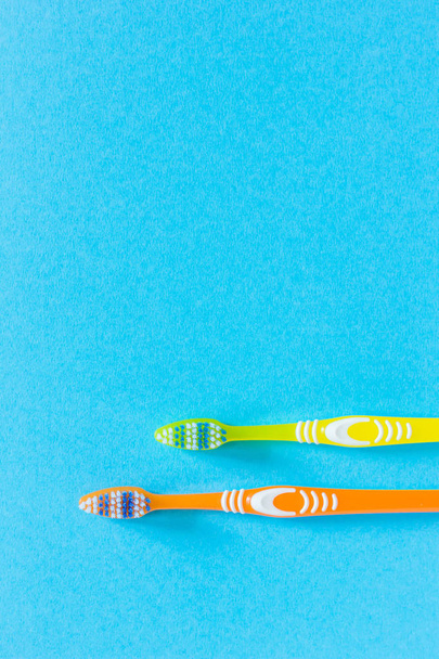 Duas escovas de dentes em um fundo azul brilhante. As escovas de dentes estão na parte inferior da foto. Escovas de dentes amarelo brilhante e laranja. Fecha. Espaço de cópia
. - Foto, Imagem
