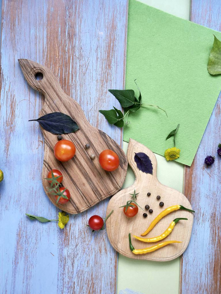 Cherry tomatoes, hot peppers, vegetables, spices on cutting boards on a textured blue wooden background. Decorative still life, top view, concept of home healthy food - Photo, Image