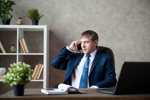 Serious businessman communicates on the phone in his office at the table - Valokuva, kuva