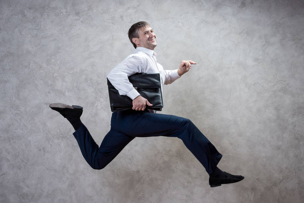 running businessman with briefcase on gray background. - 写真・画像