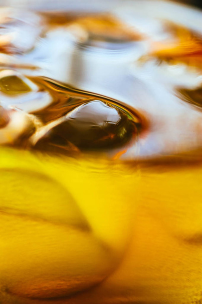 Abstract golden background, liquid drink with ice in a glass. Drinking whiskey or tequila, alcohol drinks consent, macro view. - Fotó, kép