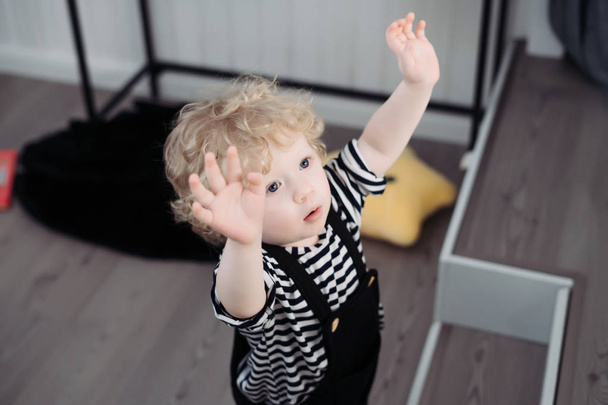 a small fair-haired child the boy is standing on the floor, raised his hands up, wants to mom - Fotoğraf, Görsel