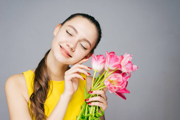 charming beautiful girl in a yellow dress smiling, closed her eyes, holds a bouquet of fragrant flowers - Fotografie, Obrázek