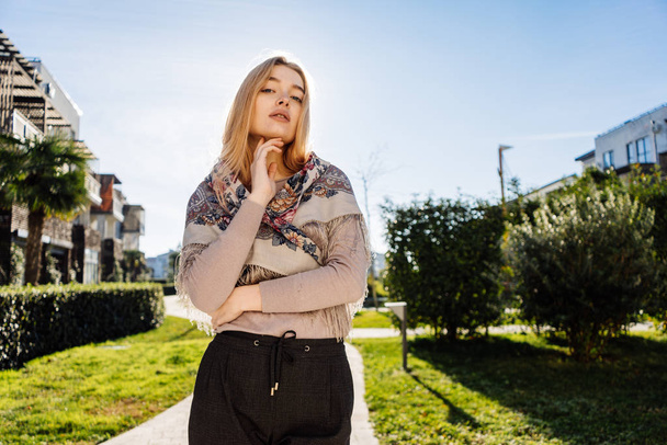 confident blond girl with a handkerchief on her shoulders posing in the rays of the spring sun - Foto, afbeelding