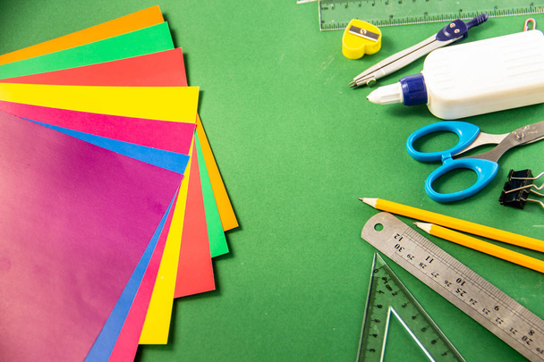 Canetas de feltro, lápis, clipes de papel, lápis de cor, réguas, cola, marcador de corretor e papel colorido em um fundo verde
 - Foto, Imagem