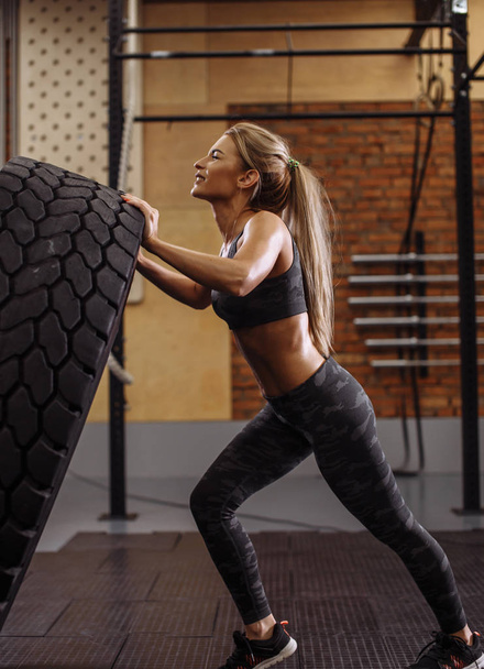 angry blond woman with closed eyes cant flip the tire. side view photo - Fotografie, Obrázek