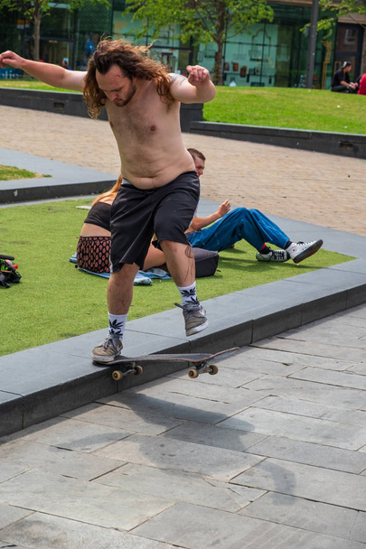 Манчестер, Великобритания - 23 июля 2018 года: Человек катается на скейтборде, как другие люди наслаждаются солнцем в жаркий летний день в центре Манчестера
 - Фото, изображение