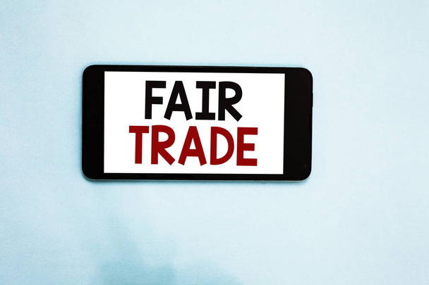 Text sign showing Fair Trade. Conceptual photo Small increase by a manufacturer what they paid to a producer Cell phone white screen over light blue background text messages apps - Photo, Image