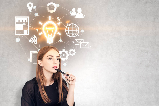 Pensive young woman with long fair hair holding a pen near her chin. A concrete wall background with glowing light bulb and business icons. Mock up - Φωτογραφία, εικόνα