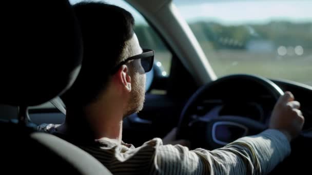 jonge knappe man is zitten in een auto alleen en ontroerend over snelweg in zonnige dag, op zoek in een rearview spiegels - Video