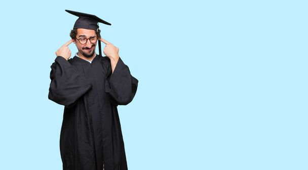young graduated man with both hands covering ears to protect them from an uncomfortable, loud, annoying noise. - Foto, Imagem
