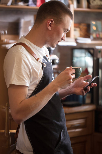 pleasant waiter is looking at the screen of the cell phone. surf the net. - Fotoğraf, Görsel