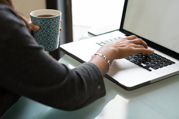 Женщина-руководитель использует ноутбук во время чашки кофе в офисе
 - Фото, изображение