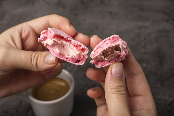 Tasty macaron is broken in half in female hands. Dark background  - Foto, imagen