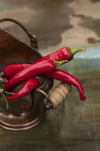 Hot peppers, fresh in a bronze pot, on the wooden background  - Foto, Imagem