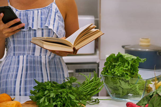 Egy fiatal nő szakácskönyvet olvas a konyhában, receptet keres. - Fotó, kép