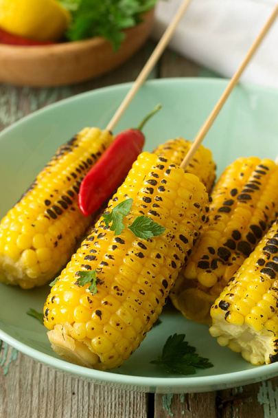 Sweet baked corn in a deep plate, served with chamichurri sauce and lemon. Rustic style, selective focus. - Фото, изображение