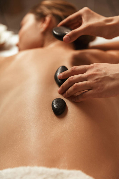 Beautiful young woman having hot stone massage in spa - Photo, Image