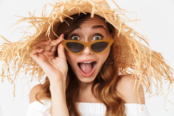 Portret close-up van opgewonden schattig vrouw 20s dragen grote stro hoed kijken camera onder zonnebril geïsoleerd op witte achtergrond - Foto, afbeelding