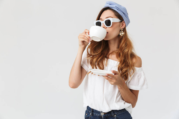 Image of european stylish woman 20s wearing sunglasses drinking tea or coffee from cup isolated over white background - Photo, Image