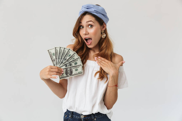 Image of excited joyful woman 20s rejoicing and holding fan of dollar money isolated over white background - Foto, Imagen