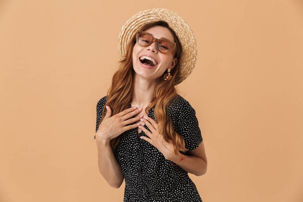 Portrait of cheerful beautiful woman wearing straw hat and sunglasses laughing isolated over beige background - Foto, Imagem