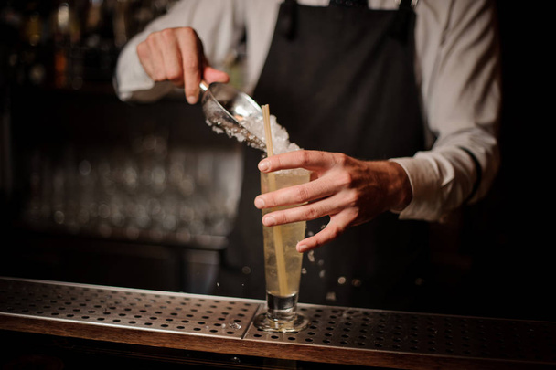 Бармен добавляет лед в бокал со свежим и вкусным кислым летним коктейлем в баре
 - Фото, изображение