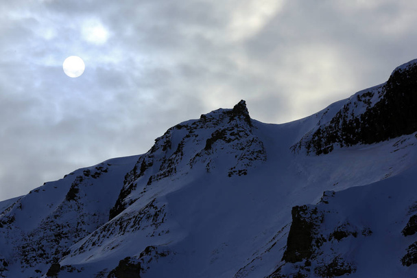 Pyöreä aurinko pilvessä, lumisella harjanteella. Huippuvuoret, Norja
 - Valokuva, kuva