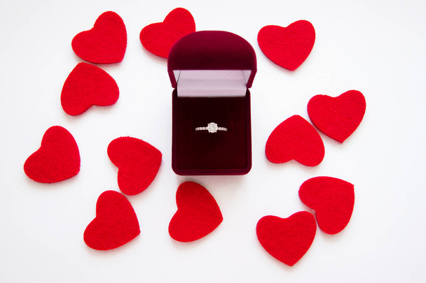 Top view of beautiful luxury wedding ring with precious stone in red velvet gift box on white backgroung with red hearts. Valentine's day marriage proposal. Present and love concept. - Фото, зображення