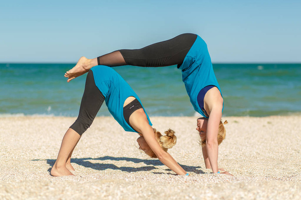 Two womans doing yoga fitness exercises on the sea beach. - Foto, Imagem