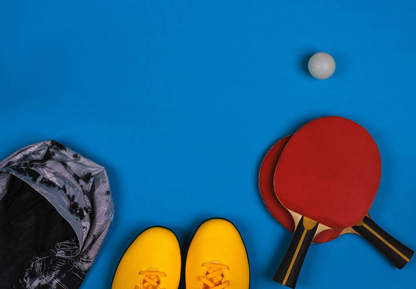 Top view on the sport composition with sneakers, jacket, tennis rocket with ball on the bright blue background - Fotografie, Obrázek