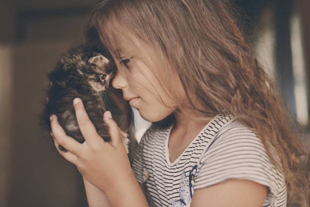 Happy cute little girl playing with a kitten at home - Фото, изображение