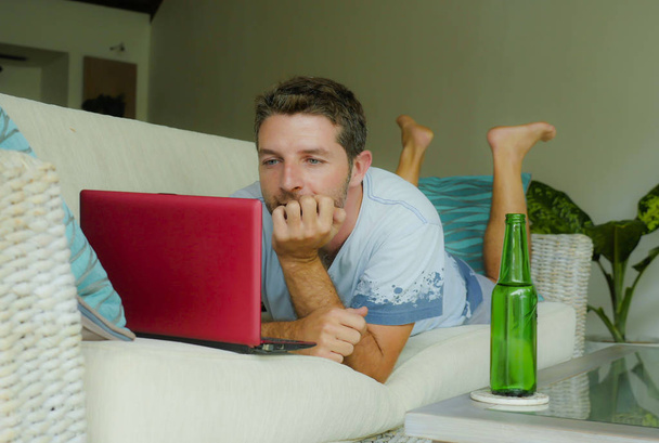 lifestyle indoors portrait of young attractive and happy man lying at home sofa couch relaxed using internet on laptop computer watching online movie or working as independent freelancer  - Foto, Imagen