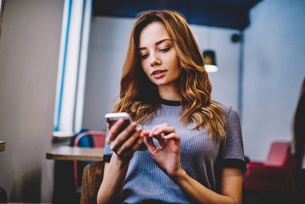 Concentrated female user reading serious text message via application on modern cellular phone, attractive hipster girl typing email during communicate with followers in social networks via smartphone - Fotoğraf, Görsel