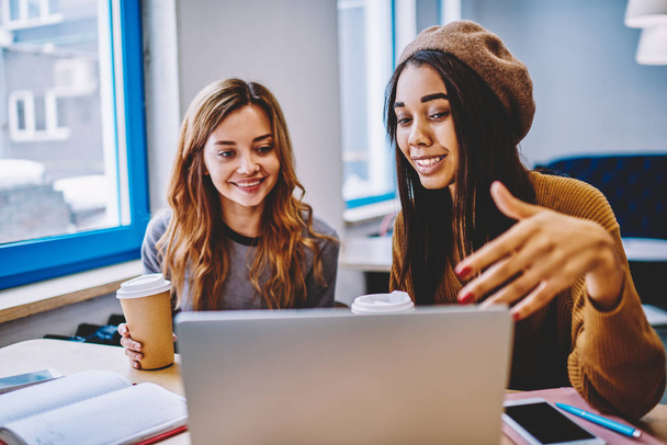 Szczęśliwy wielokulturowym kobiet zakupy online razem przy użyciu połączenia Wi-Fi na urządzeniu laptopa, udany uśmiechający się dziewczyny hipster oglądania filmu pozytywne komedia na netbook w pomieszczeniu przerwa na kawę - Zdjęcie, obraz