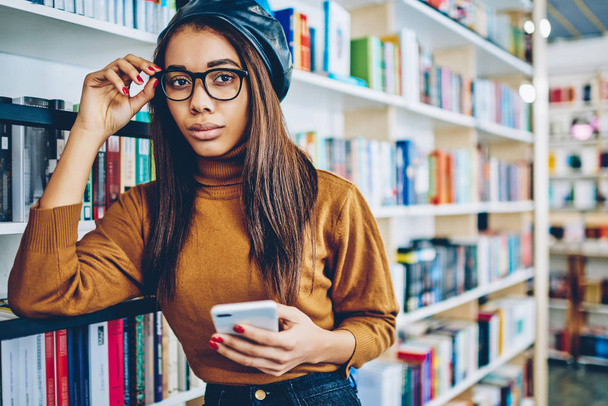 Half length portrait of african stylish hipster girl holding smartphone and updating profile on internet page, millennial attractive woman checking notification on cellular phone with 4g connection - Photo, Image