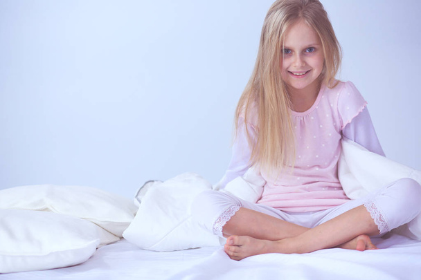Little girl in the bedroom is sitting on the bed. Little girl is wearing a pajamas and sitting in bed . - Zdjęcie, obraz