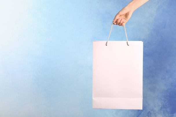 Woman holding paper shopping bag on color background - Foto, imagen