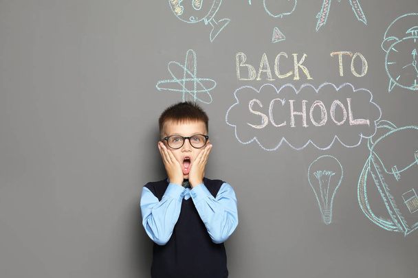 Little child in uniform near drawings with text BACK TO SCHOOL on grey background - Fotoğraf, Görsel