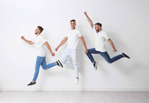 Group of young men in jeans jumping near light wall - Foto, Imagem