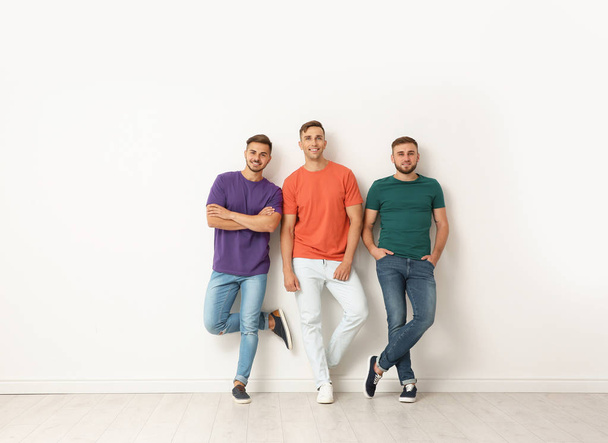 Group of young men in jeans and colorful t-shirts near light wall - Foto, imagen