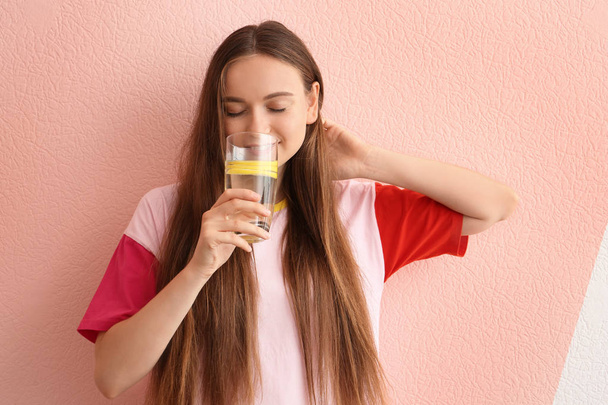 Young woman drinking lemon water on color background - 写真・画像